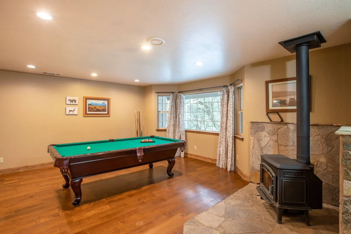 A relaxed living area with a pool table, wood-burning stove, and windows adorned with curtains. The space encourages sociable activities, with features that support both friendly games and intimate conversations by the stove.