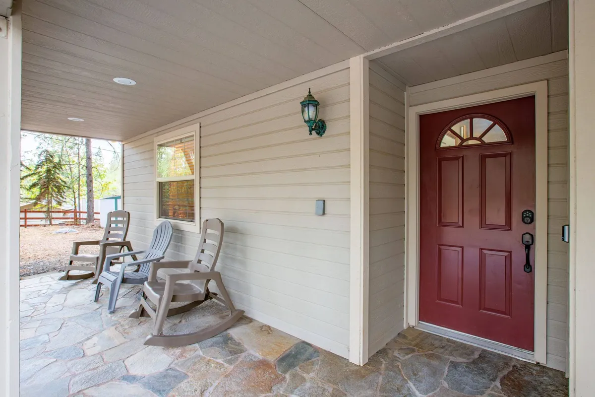 This image features a welcoming interior space with a prominent red front door, rustic stone flooring, and cozy rocking chairs. The area exudes a sense of arrival and transition, providing a comfortable threshold between the outdoors and the rest of the home.