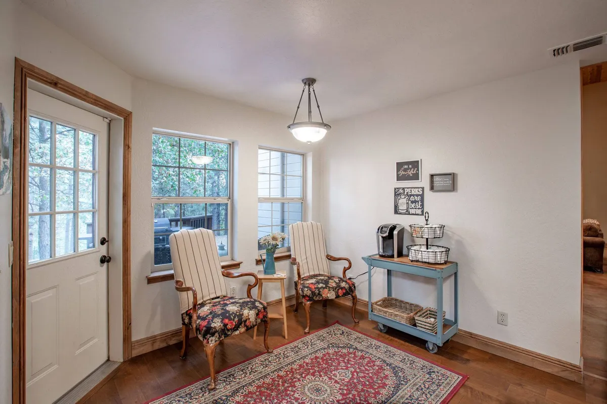 A cozy breakfast nook with two vintage armchairs set around a decorative rug, beside a coffee station with baskets. Large windows flood the space with natural light, creating an inviting spot for morning coffee, reading, or casual conversation.