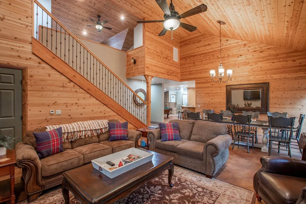 An interior view featuring a wooden staircase, a plush sofa set, and a visible dining area under a chandelier. The space has a warm, welcoming atmosphere ideal for family gatherings or intimate dinners.
